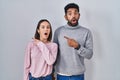 Young hispanic couple standing together surprised pointing with finger to the side, open mouth amazed expression Royalty Free Stock Photo