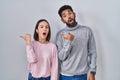 Young hispanic couple standing together surprised pointing with hand finger to the side, open mouth amazed expression Royalty Free Stock Photo