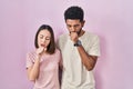 Young hispanic couple together over pink background feeling unwell and coughing as symptom for cold or bronchitis Royalty Free Stock Photo