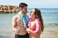 Young hispanic couple tourists wearing hawaiian lei using smartphone at seaside Royalty Free Stock Photo