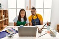 Young hispanic couple using laptop sitting on the table at art studio scared and amazed with open mouth for surprise, disbelief Royalty Free Stock Photo