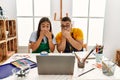 Young hispanic couple using laptop sitting on the table at art studio shocked covering mouth with hands for mistake Royalty Free Stock Photo