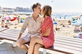 Young hispanic couple on vacation kissing sitting on bench at the beach Royalty Free Stock Photo