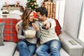 Young hispanic couple watching movie and eating popcorn sitting on the sofa at home Royalty Free Stock Photo