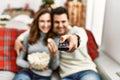 Young hispanic couple watching movie and eating popcorn sitting on the sofa at home Royalty Free Stock Photo