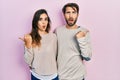 Young hispanic couple wearing casual clothes surprised pointing with hand finger to the side, open mouth amazed expression Royalty Free Stock Photo