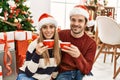 Young hispanic couple wearing christmas hat drinking coffee at home Royalty Free Stock Photo