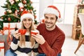 Young hispanic couple wearing christmas hat drinking coffee at home Royalty Free Stock Photo