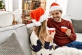 Young hispanic couple wearing christmas hat drinking coffee sitting on the sofa at home Royalty Free Stock Photo