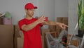 Young hispanic courier with smartphone points finger inside building interior amid stacks of moving boxes; focus Royalty Free Stock Photo