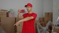 Young hispanic courier with smartphone points finger inside building interior amid stacks of moving boxes; focus Royalty Free Stock Photo