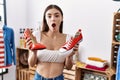 Young hispanic customer woman holding high heel shoes and sneaker afraid and shocked with surprise and amazed expression, fear and