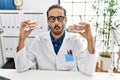 Young hispanic dentist man holding denture with orthodontic braces making fish face with mouth and squinting eyes, crazy and