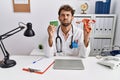 Young hispanic doctor man holding female genital organ and birth control pills puffing cheeks with funny face Royalty Free Stock Photo