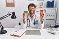 Young hispanic doctor man holding female genital organ and birth control pills smiling and laughing hard out loud because funny Royalty Free Stock Photo