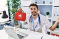 Young hispanic doctor man holding first aid kit celebrating achievement with happy smile and winner expression with raised hand Royalty Free Stock Photo