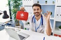 Young hispanic doctor man holding first aid kit doing ok sign with fingers, smiling friendly gesturing excellent symbol Royalty Free Stock Photo