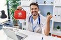 Young hispanic doctor man holding first aid kit screaming proud, celebrating victory and success very excited with raised arm Royalty Free Stock Photo