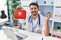 Young hispanic doctor man holding first aid kit smiling happy pointing with hand and finger to the side Royalty Free Stock Photo