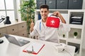 Young hispanic doctor man holding first aid kit smiling happy and positive, thumb up doing excellent and approval sign Royalty Free Stock Photo