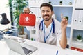 Young hispanic doctor man holding first aid kit smiling with an idea or question pointing finger with happy face, number one Royalty Free Stock Photo