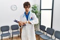 Young hispanic doctor man at waiting room checking the time on wrist watch, relaxed and confident Royalty Free Stock Photo