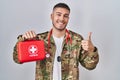 Young hispanic doctor wearing camouflage army uniform holding first aid kit smiling happy and positive, thumb up doing excellent Royalty Free Stock Photo