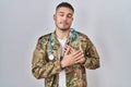 Young hispanic doctor wearing camouflage army uniform smiling with hands on chest, eyes closed with grateful gesture on face