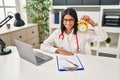 Young hispanic doctor woman holding alarm clock at the clinic looking positive and happy standing and smiling with a confident Royalty Free Stock Photo