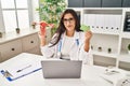 Young hispanic doctor woman holding anatomical female genital organ and birth control pills relaxed with serious expression on