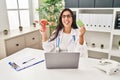 Young hispanic doctor woman holding anatomical female genital organ and birth control pills sticking tongue out happy with funny Royalty Free Stock Photo