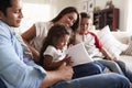 Young Hispanic family of four sitting on the sofa reading book together in their living room Royalty Free Stock Photo