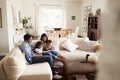 Young Hispanic family sitting on sofa reading a book together in the living room, seen from doorway Royalty Free Stock Photo