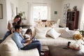 Young Hispanic Family Sitting On Sofa Reading A Book Together In Their Living Room