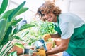 Young hispanic gardener smiling happy caring plants using watering can at terrace