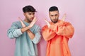 Young hispanic gay couple standing over pink background rejection expression crossing arms doing negative sign, angry face Royalty Free Stock Photo