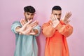 Young hispanic gay couple standing over pink background rejection expression crossing arms and palms doing negative sign, angry Royalty Free Stock Photo