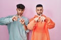 Young hispanic gay couple standing over pink background rejection expression crossing fingers doing negative sign Royalty Free Stock Photo