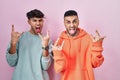 Young hispanic gay couple standing over pink background shouting with crazy expression doing rock symbol with hands up Royalty Free Stock Photo