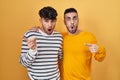 Young hispanic gay couple standing over yellow background surprised pointing with finger to the side, open mouth amazed expression Royalty Free Stock Photo