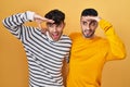 Young hispanic gay couple standing over yellow background very happy and smiling looking far away with hand over head Royalty Free Stock Photo