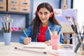 Young hispanic girl artist listening to music drawing on notebook at art studio Royalty Free Stock Photo