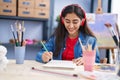 Young hispanic girl artist listening to music drawing on notebook at art studio Royalty Free Stock Photo