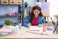 Young hispanic girl artist listening to music drawing on notebook at art studio Royalty Free Stock Photo