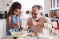 Young Hispanic girl and her grandad whisking cake mixture together at the kitchen table, close up