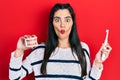 Young hispanic girl holding electric toothbrush and denture making fish face with mouth and squinting eyes, crazy and comical