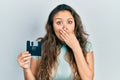 Young hispanic girl holding floppy disk covering mouth with hand, shocked and afraid for mistake Royalty Free Stock Photo