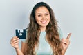 Young hispanic girl holding floppy disk smiling happy pointing with hand and finger to the side Royalty Free Stock Photo