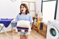 Young hispanic girl holding folded laundry angry and mad screaming frustrated and furious, shouting with anger Royalty Free Stock Photo