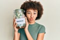 Young hispanic girl holding jar with savings looking at the camera blowing a kiss being lovely and sexy Royalty Free Stock Photo